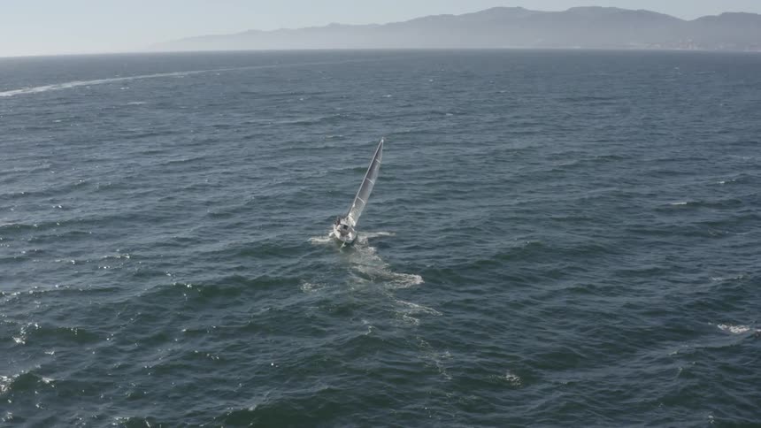 A sailboat cuts through the ocean waves on a sunny day