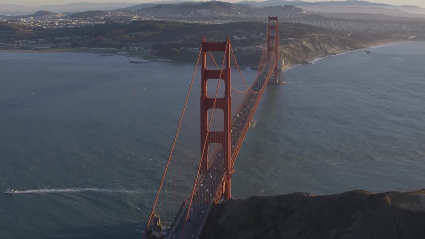 Cars traveling through golden gate bridge as a boat passes by underneath