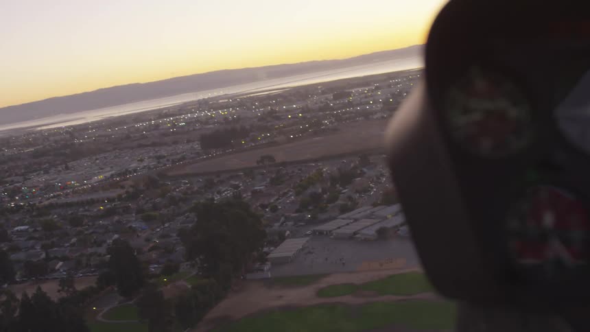A helicopter flies over a suburban area toward a circular landing pad