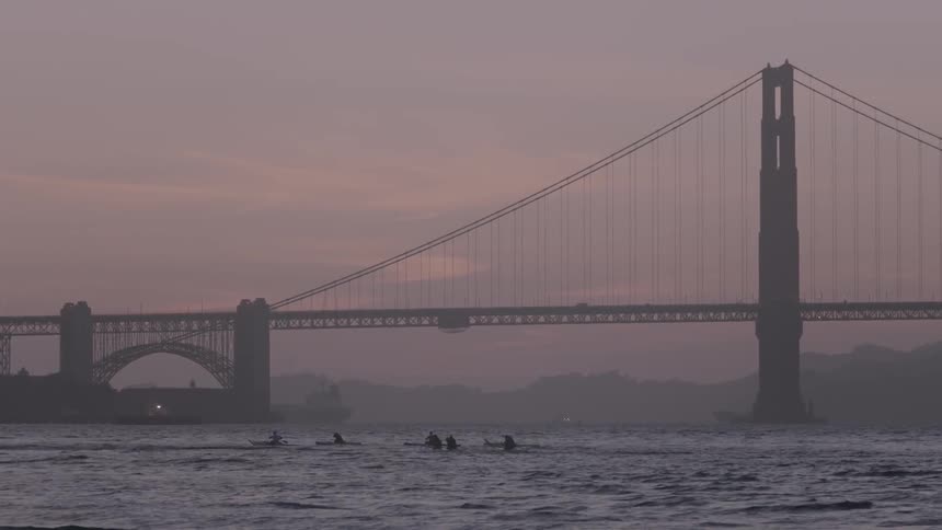 People paddle in kayaks near a city bridge