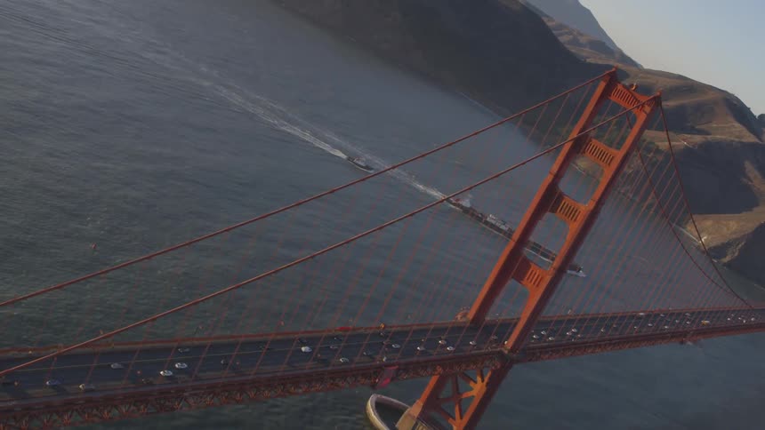 Cars travel over the golden gate bridge with ships floating nearby