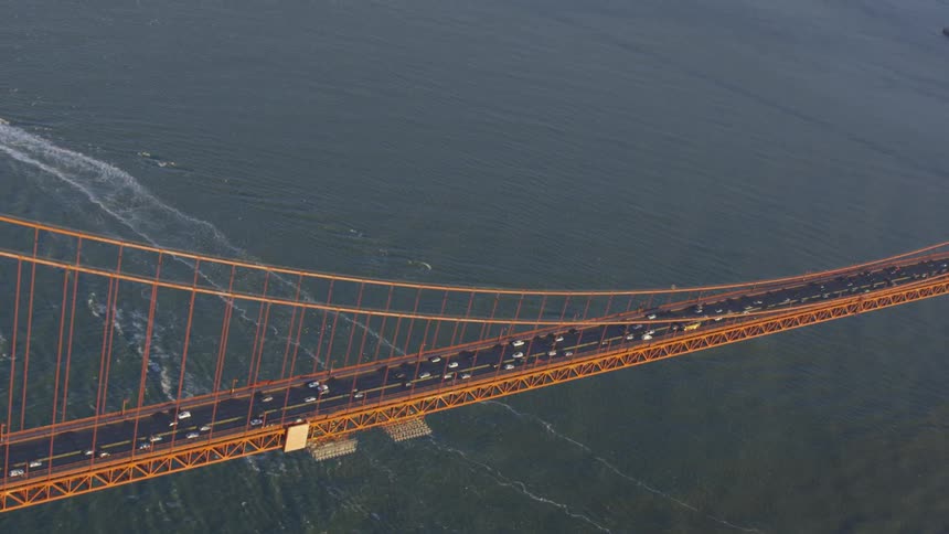 Cars travel in both directions over the golden gate bridge with boat wakes underneath