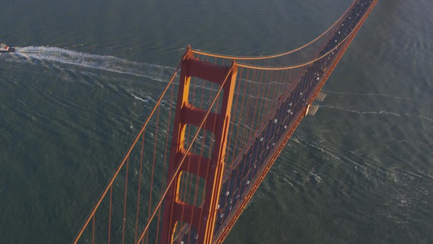 Twisting aerial of boat traveling under the golden gate bridge