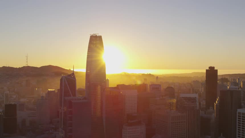 A city skyline is viewed at low sun with the ocean on the horizon