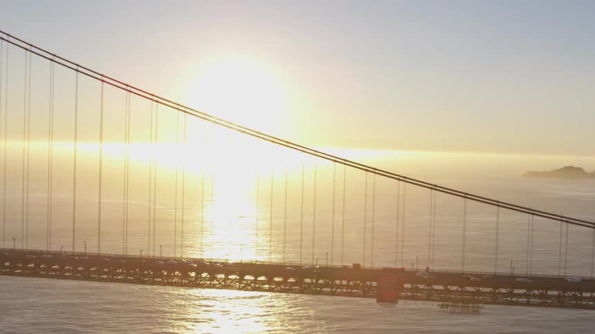The sun sets over the ocean as cars travel in both directions over a bridge
