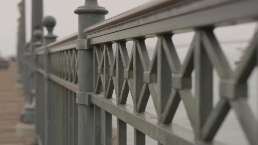 A ship in the ocean is visible through the fence on a pier on a cloudy day