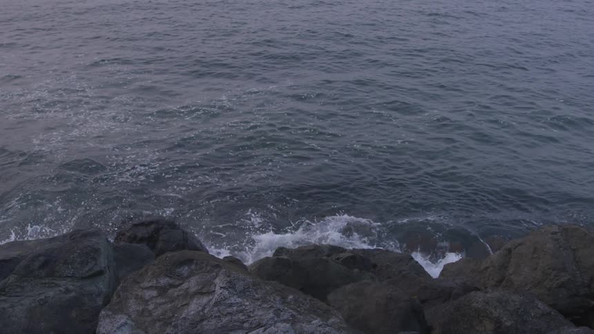 Waves hit rocks making foam at dusk