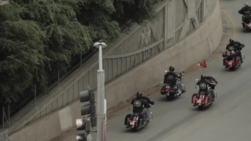 A group of motorcycles turn and merge with cars and traffic