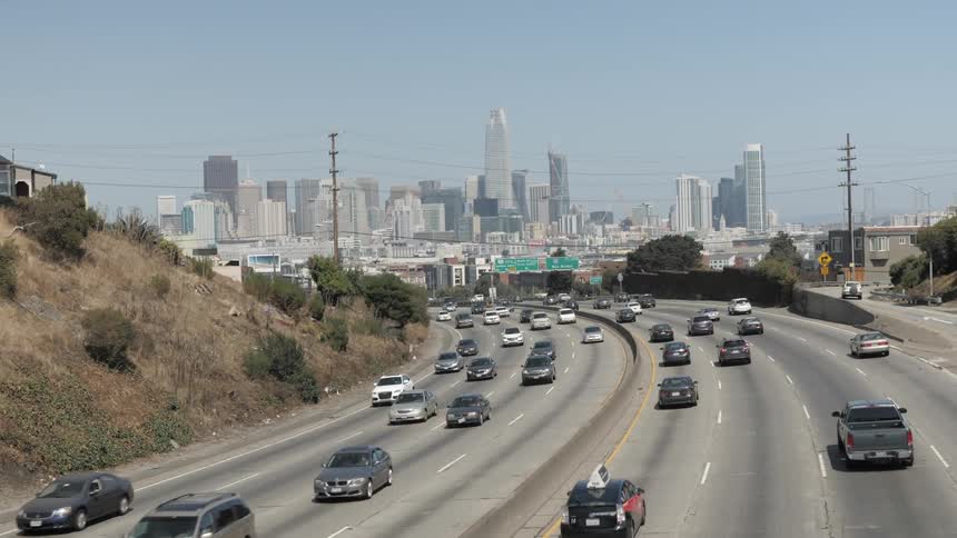 A city skyline as seen from a whole in a fence on top of an overpass