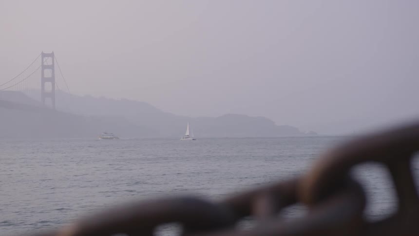 A sailboat sailing through the fog in a bay