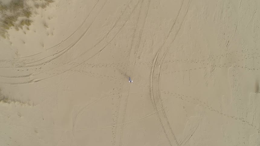 Person walks across track covered sand during the day