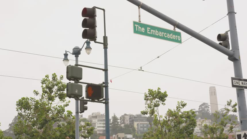 Traffic passing by a street corner with a sign titled the embarcadero
