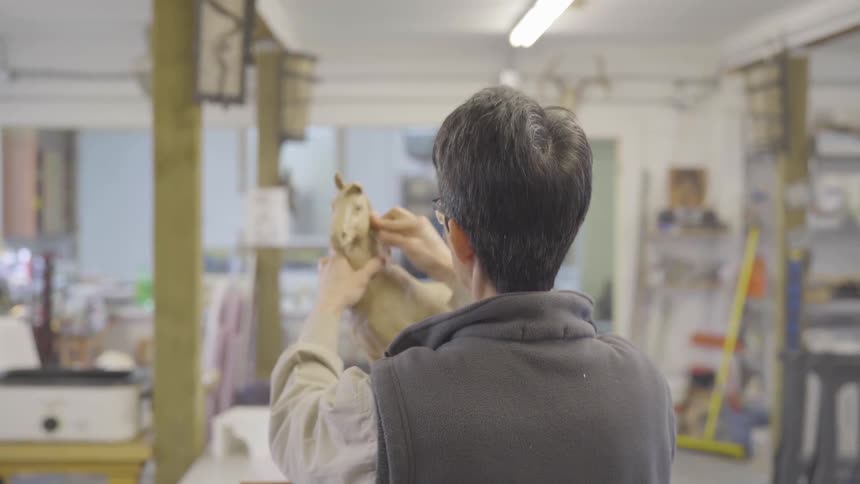 An artist shapes the mane of a clay horse being sculpted in their studio
