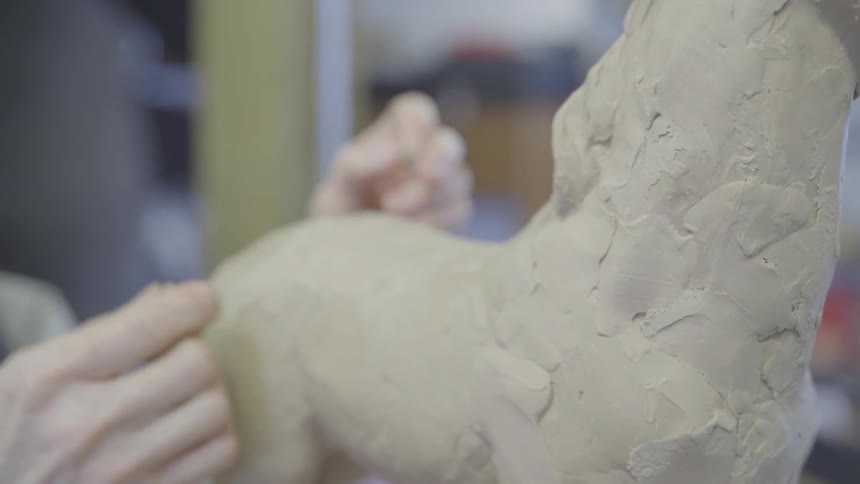 An artist presses and smooths clay onto a horse sculpture