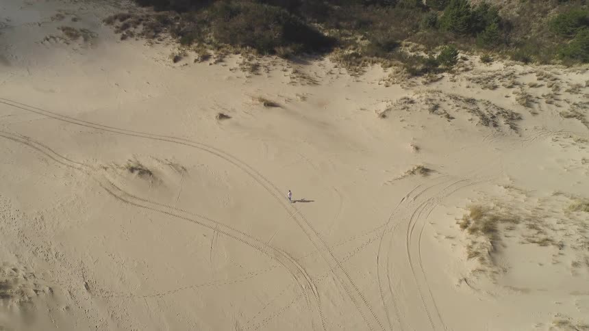 Person walking through sandy area surrounded by tire tracks
