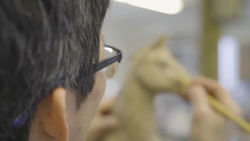 A male artist sculpts a horse statue in a studio