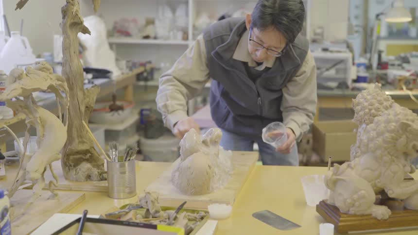 Man putting clay onto a sculpture that he is working on in a studio