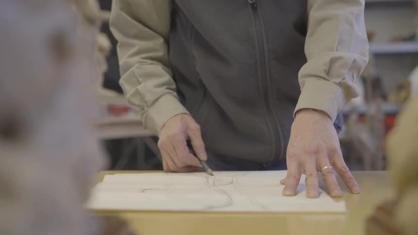 A man sketches on a piece of paper on a table with a pencil