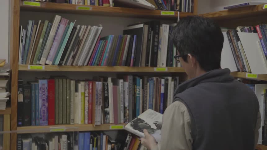 Male walking into room towards bookshelf and pulling out a book