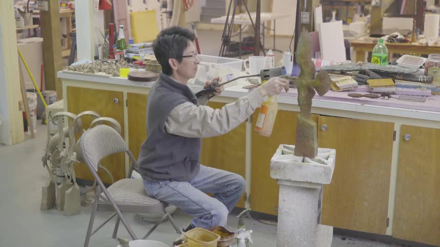 Asian man using spraying and using a torch on a bird sculpture in a workshop