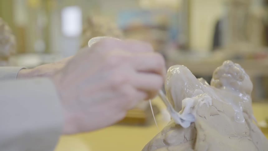 A person applying glaze with a paintbrush onto clay