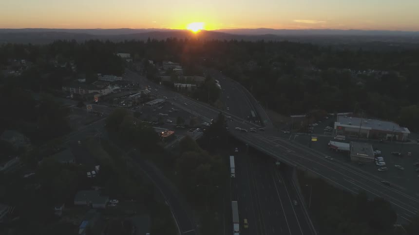 Cars and trucks travel on a highway and overpass at sunset