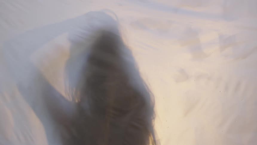 A silhouetted woman rubs her hands through her hair behind a sheet