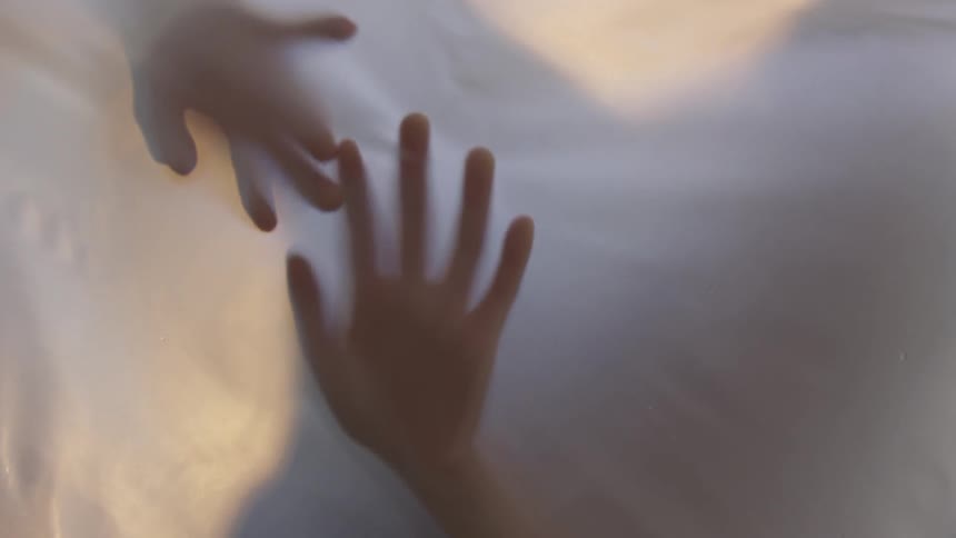 Hands are seen pushing and gliding along on a ghostly thin piece of translucent fabric