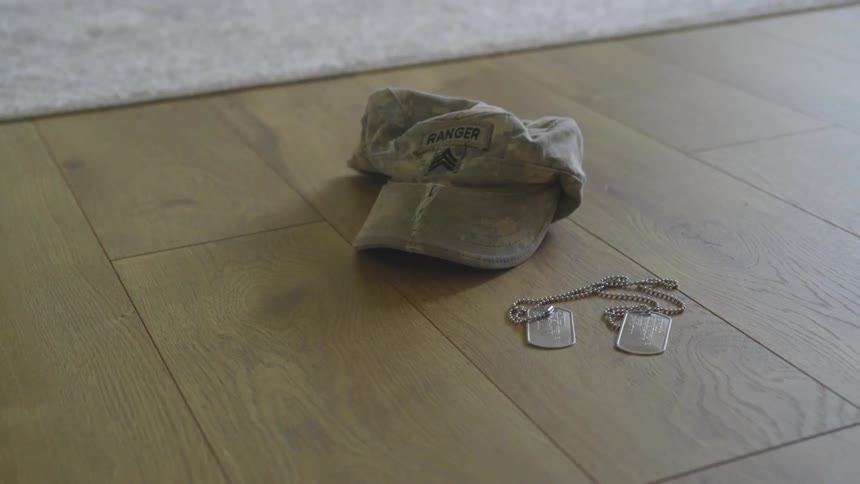 Service dog tags lie on a wooden floor next to a ranger cap