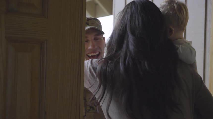 Woman holding baby in her arms opens the door and hugs the soldier by day