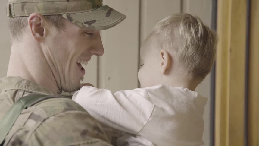 A man in a military uniform kisses a child