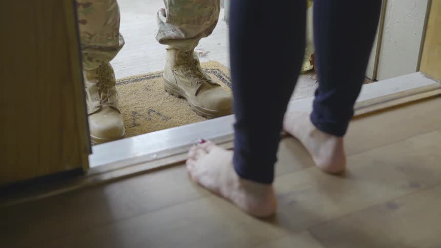 Barefoot woman standing on threshold greeting a military person