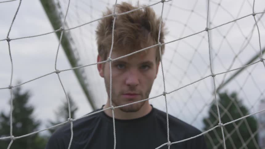 A young man standing inside of a soccer net outside