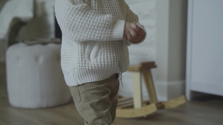 A child standing in a house playing with a silver dog tag necklace