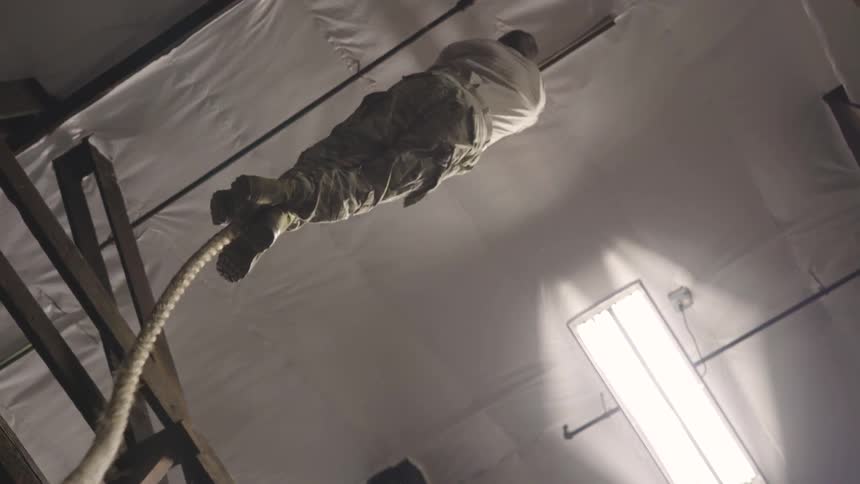 Caucasian male is climbing the rope in military type pants and a t shirt