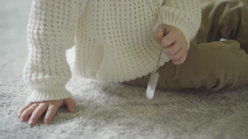 Toddler sits down on the carpet and plays with the dog tag at house