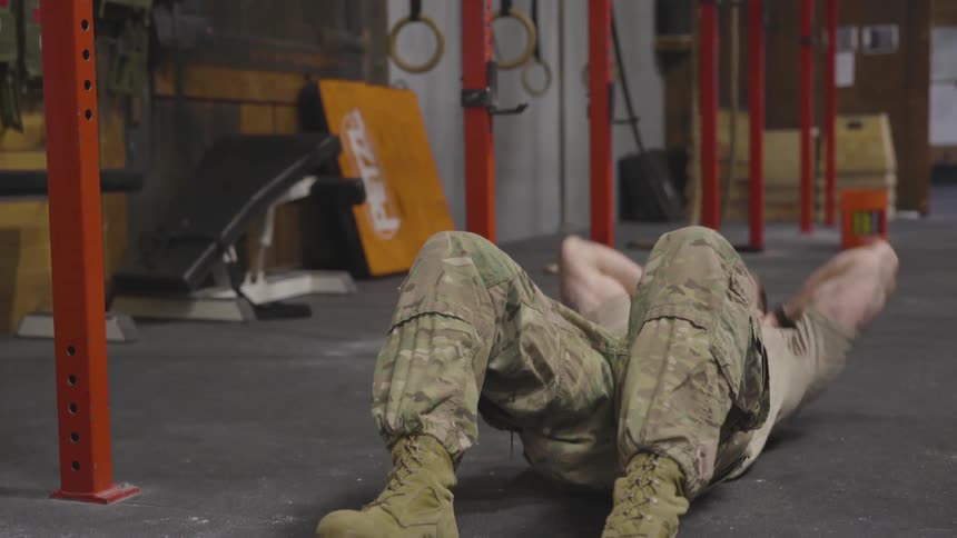 Soldier is doing sit ups on concrete ground at gym by day