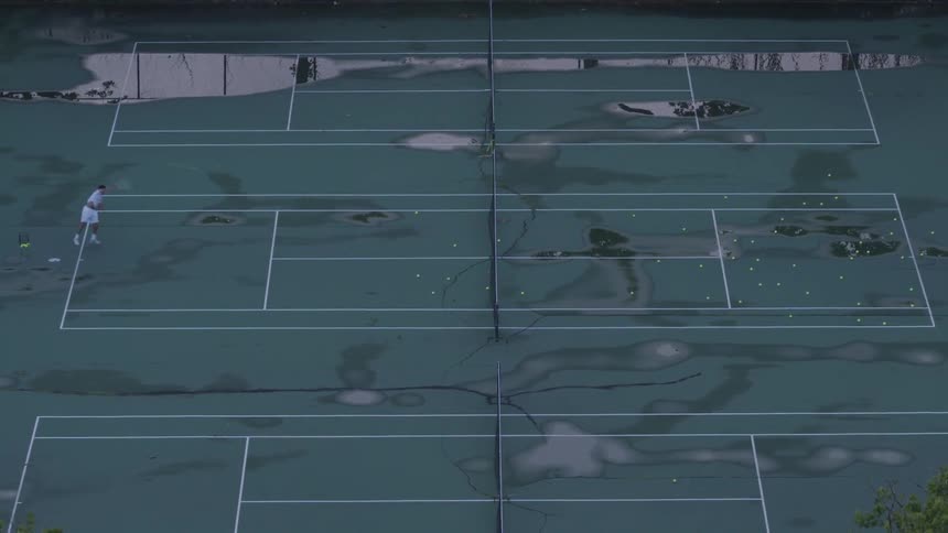 Elevated view of a man practicing his serving on a wet tennis court