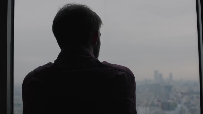 A man gazes through a window overlooking a city