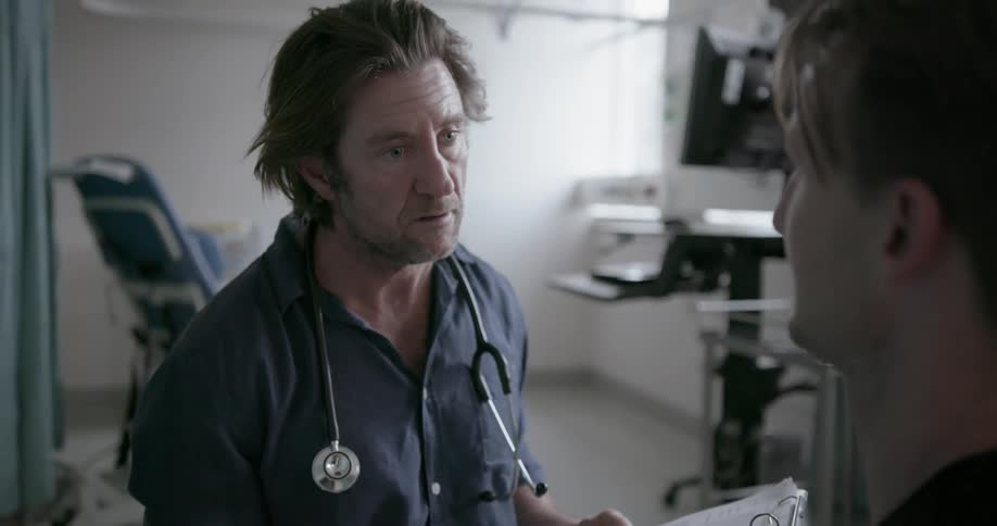 Doctor is talking to patient in hospital room and writing on clipboard