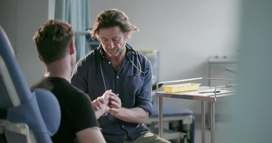 A doctor talks to a patient then examines his hand