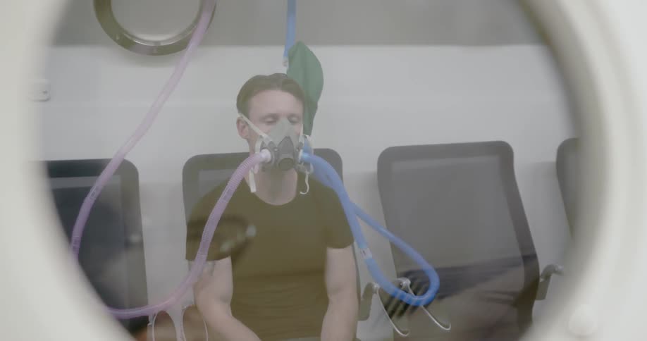 A man sits in an air pressure cabin with a mask on