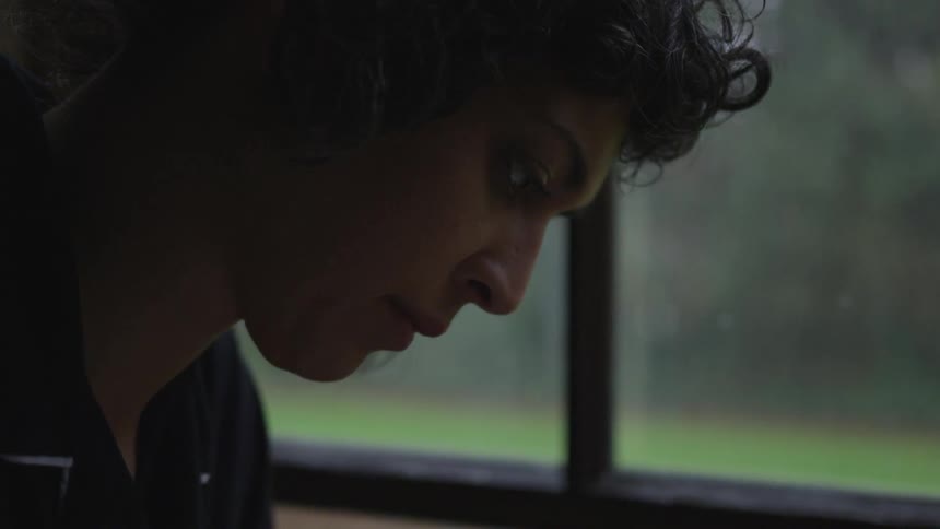 Teen looks down thoughtfully next to a window