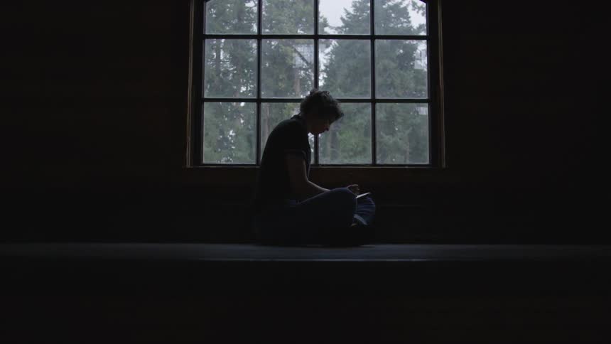 Child sits in a dark room in front of a window