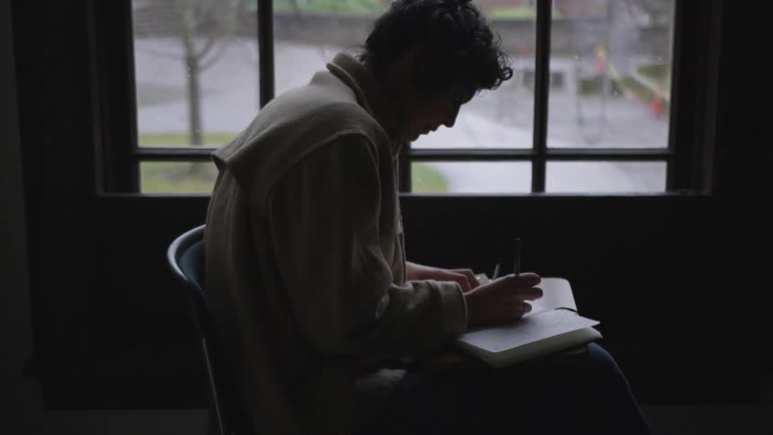Person sits in front of a window writing in a notebook