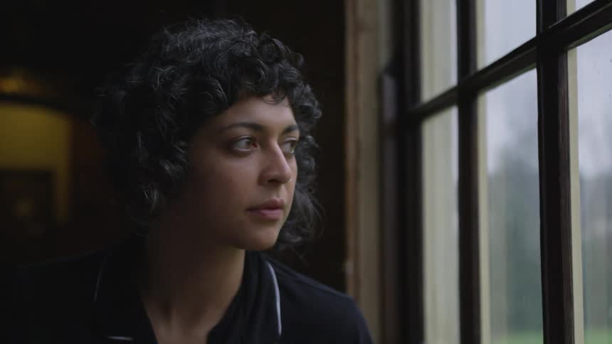 A curly haired woman standing near and gazing out a window during the day