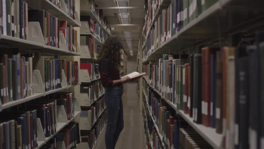 A woman is in a library looking at a book