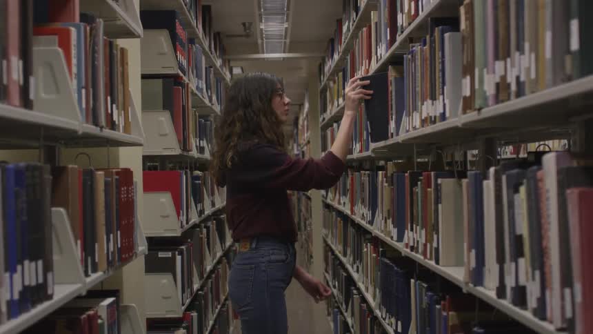 Woman is looking at books on shelf in library