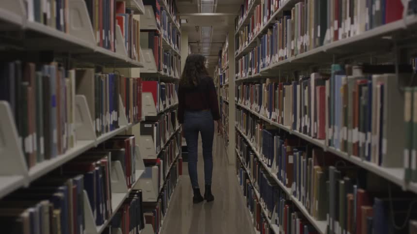 A woman walking through rows of books in a library