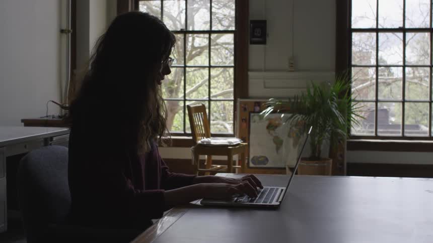 Woman sits at a table typing on a laptop